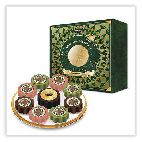 A decorative green and gold box labeled "Wish Upon The Moon" with a circular pattern and a full moon illustration, placed behind a plate of nine mooncakes in pink, green, and brown colors, each featuring intricate designs on top.
